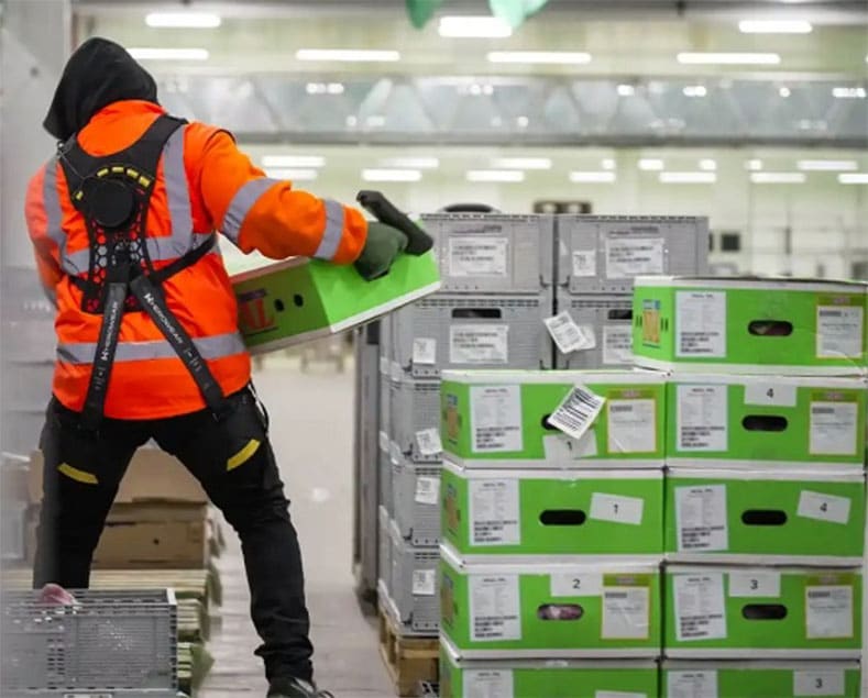 MOV warehouse worker handling crates while wearing a HeroWear Apex 2 back support exosuit.