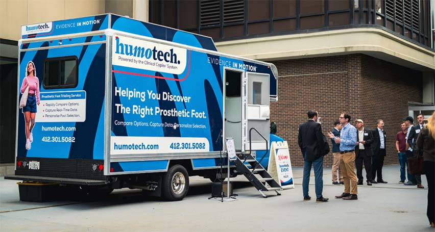 Blue Humotech mobile clinic vehicle with people standing beside it.